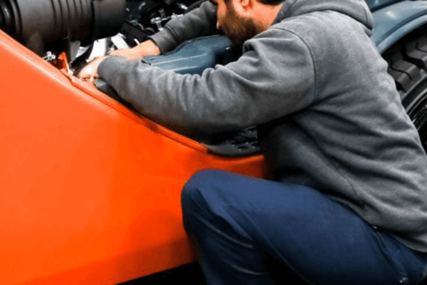 A man works on the engine of an orange car, focusing on maintenance and repairs.