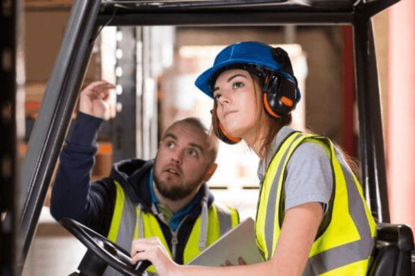 A man and woman in safety vests inspect a forklift, emphasizing proactive safety and maintenance practices.